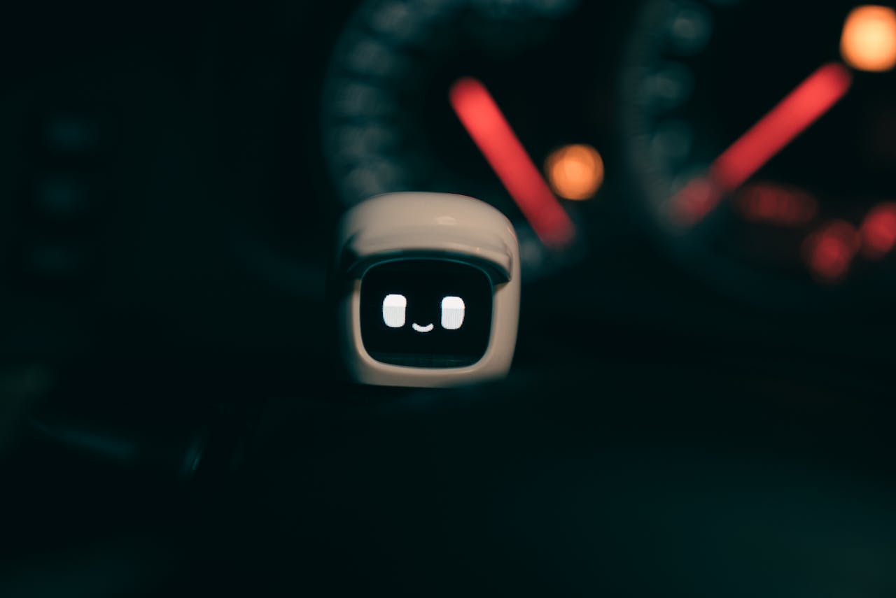 A small robotic figure with a smiling face on a car dashboard, lit by blurred speedometer lights at night.